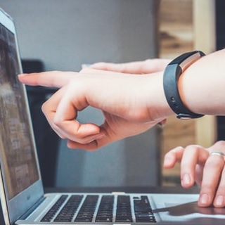 A hand pointing toward a computer screen.