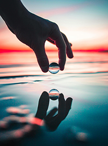 hand pinching marble over water at sunset