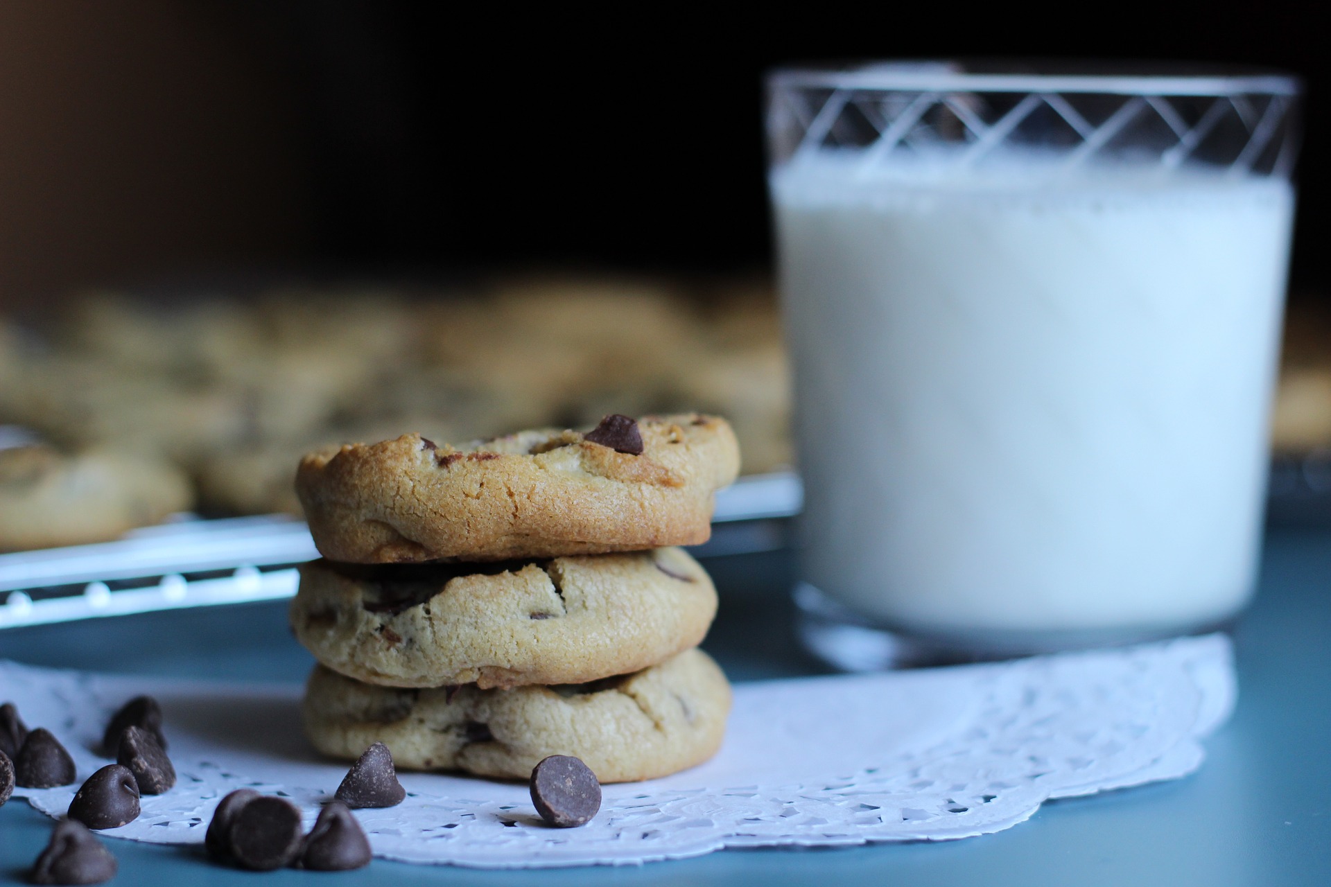 stack of 3 chocolate chip cookies on a folded doilie with a glass of milk beside