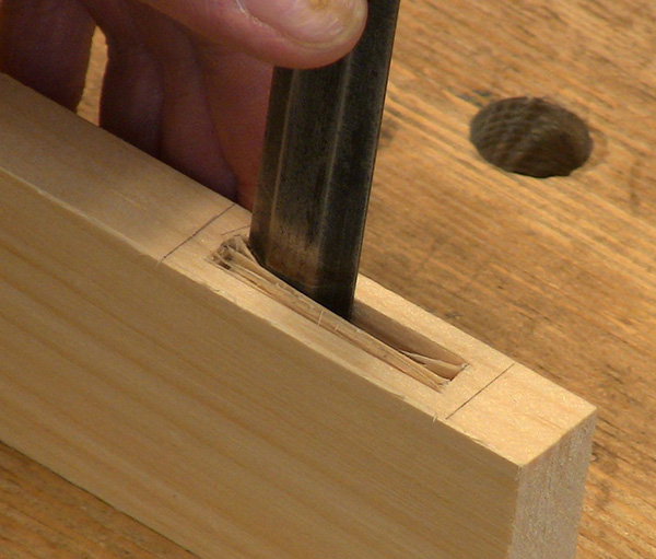 A hand chiseling wood from a mortise.