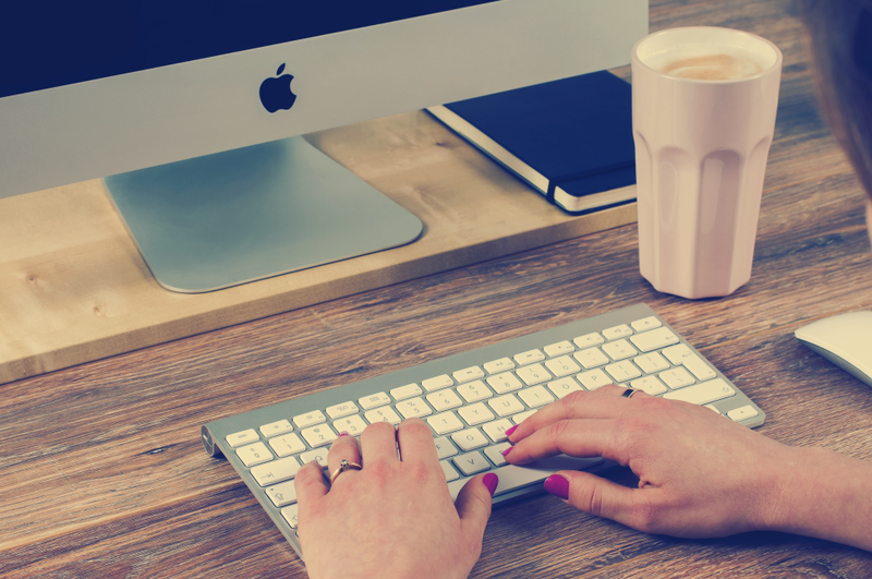 someone's hands typing on a keyboard in front of a desktop monitor
