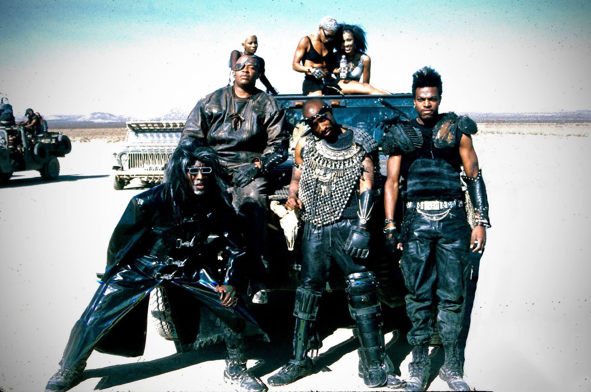 photo of Dr.Dre and Roger Troutman on left, center Tupac Shakur, right Chris Tucker in the desert leaning on a jeep